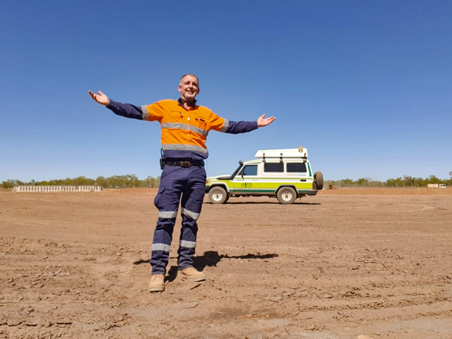 Man in hi-viz wear standing with arms stretched out in a remote setting 