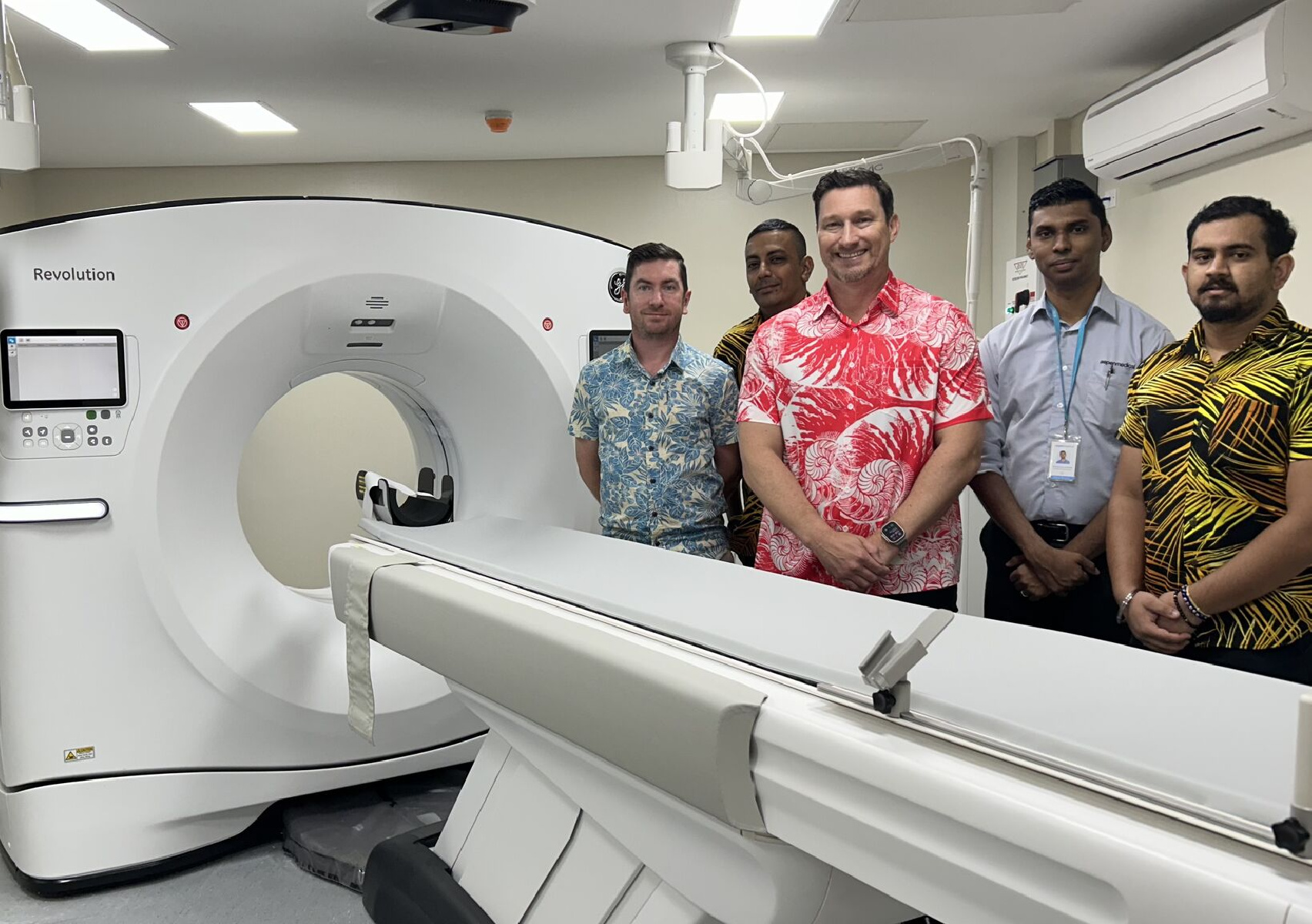 Five men in a hospital stand beside a CT scanner