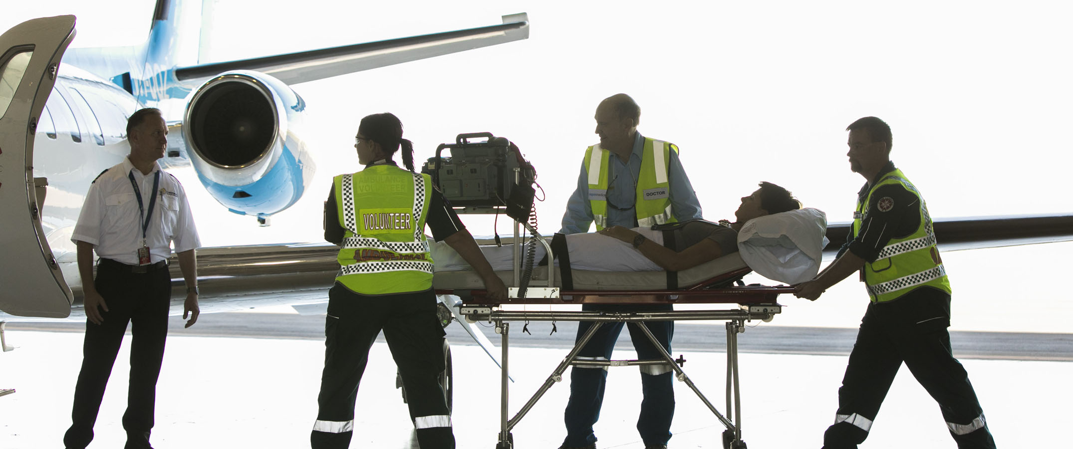 Photo of clinicians wheeling a patient on a gurney onto a plane.