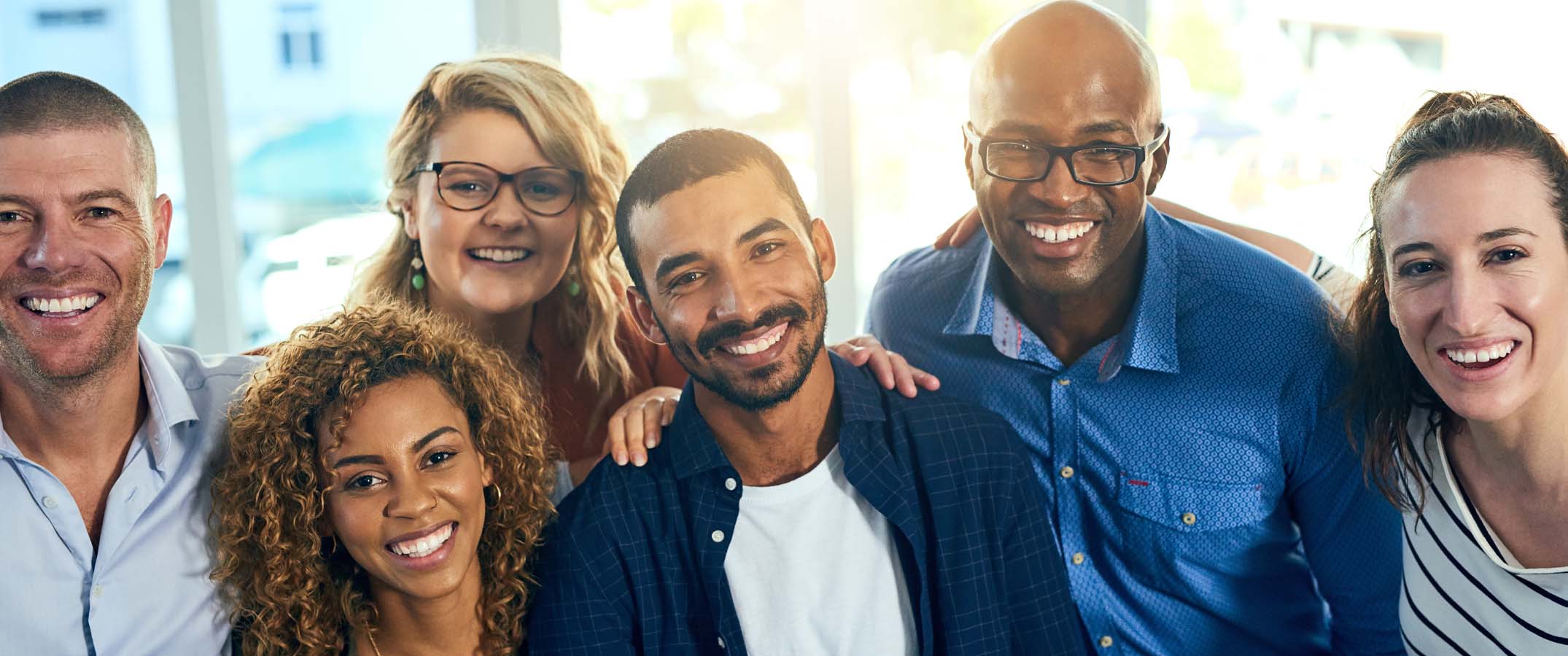 Image of three women and three men, smiling natural at the camera as a group.