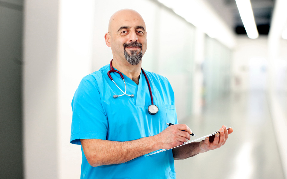 Photo of male Emirates doctor wearing blue scrubs and looking straight ahead.
