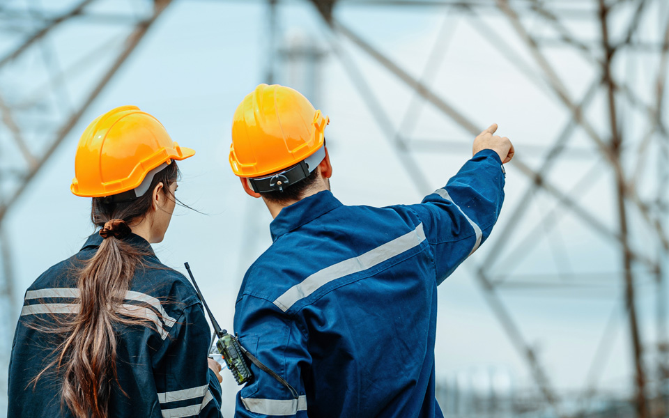 Photo shows the back of two energy workers wearing yellow hard hats.