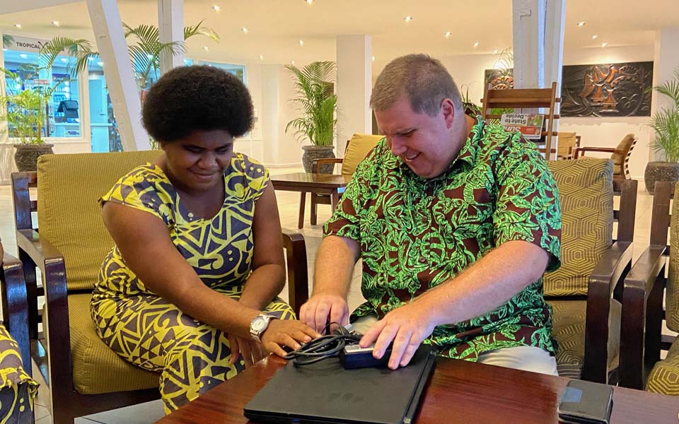 Photo of Naomi sitting down with Ben Clare and they're both reaching for a laptop on the table and smiling.
