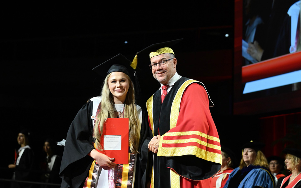 Foundation scholarship recipient, Dr Tahni Derbin receiving her award on stage in her graduation gown and hat. 