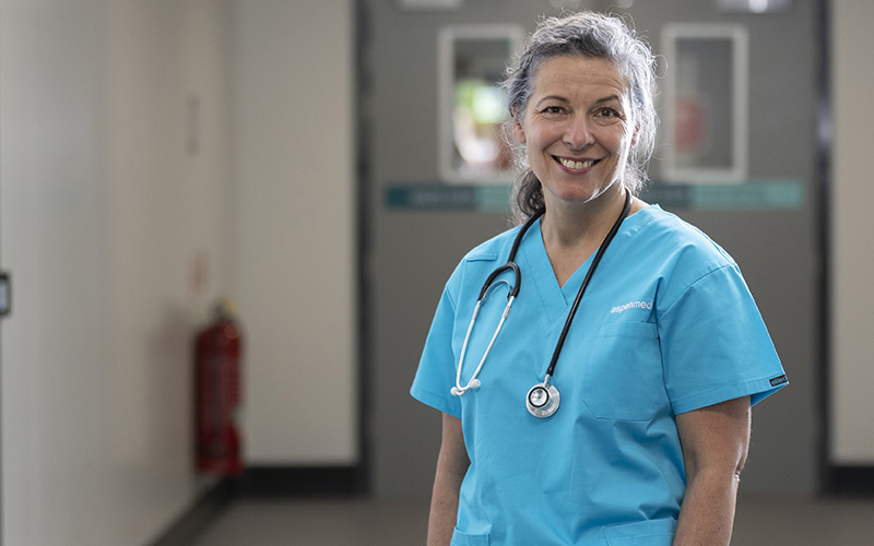 This photo shows a female clinician in a hospital wearing blue scrubs and smiling at the camera.