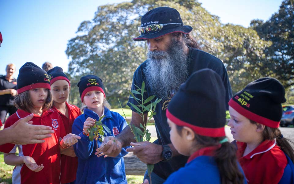 Photo of Malpa team member engaging with a group of children in school uniform, wearing Malpa beenies.