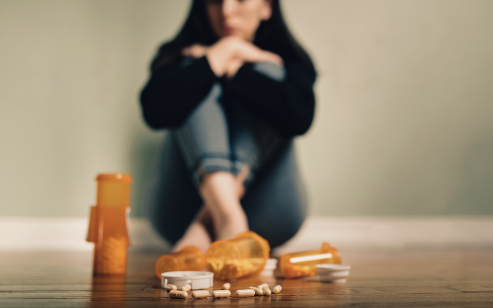 Photo of a young women looking nervously at some pills on the floor.