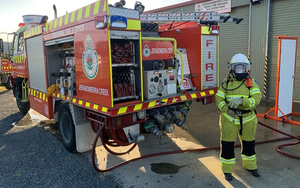 Photo of Ruth dressed in her fire fighting uniform and standing next to a fire truck.