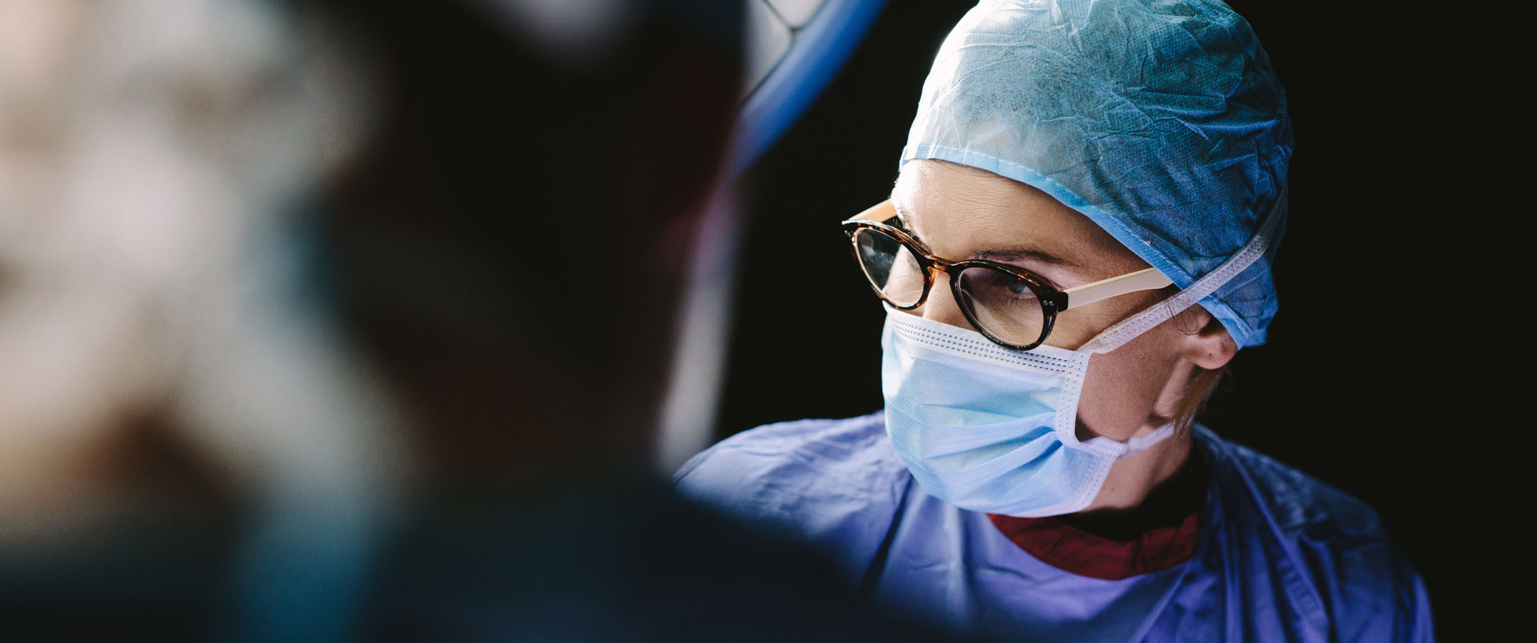 Photo of a surgical scene focused on the female surgeon in a moody setting.