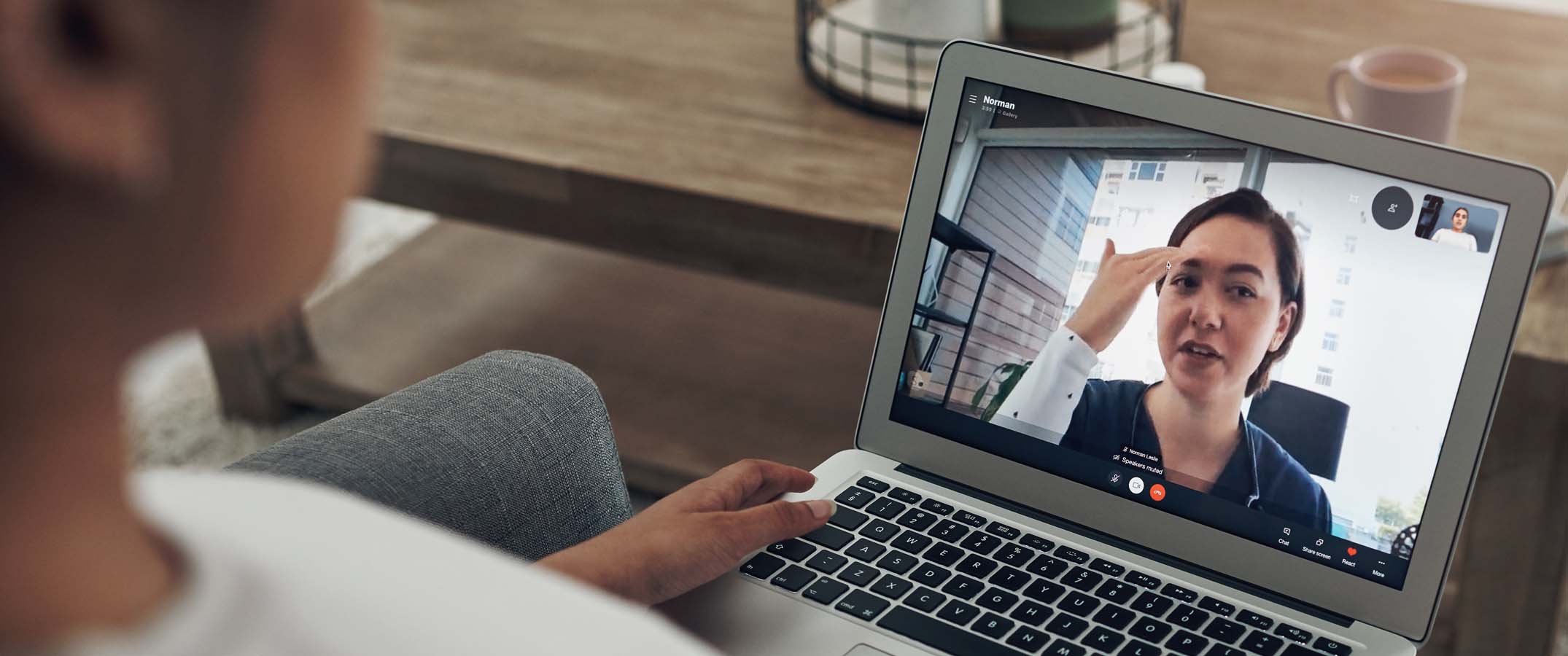 Photo of a female clinician on a laptop screen held by a person out of shot.