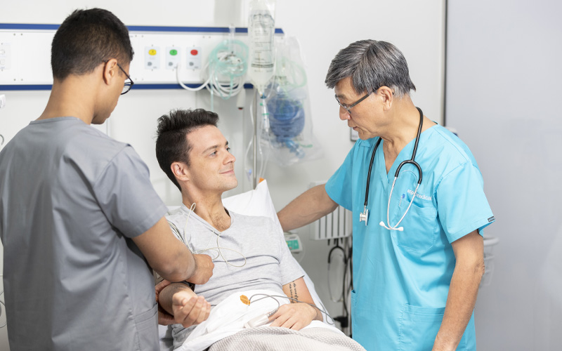 Photo of two clinicians monitoring and talking to a patient in the bed.