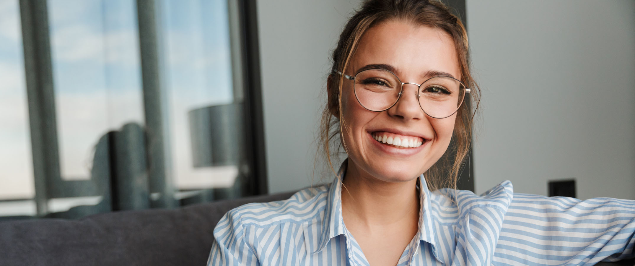 Image of a young women in glasses, smiling at the camera, looking happpy.