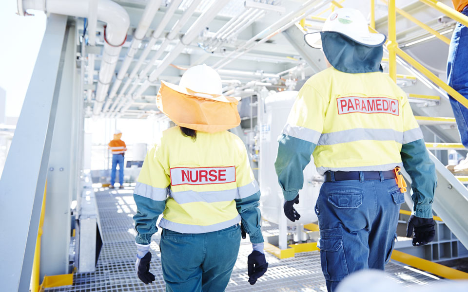 Photo of two Aspen Medical clinicians wearing full site safety gear and walking away from the camera on a client site.