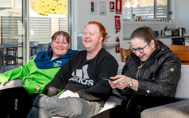 Photo of three Project Independence homeowners sitting on the couch together, having a laugh.