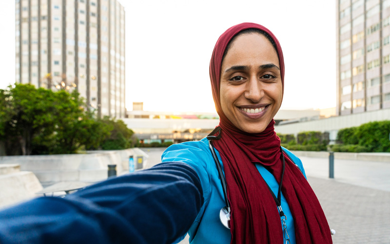 Photo shows a female clinician standing outside taking a selfie photo.