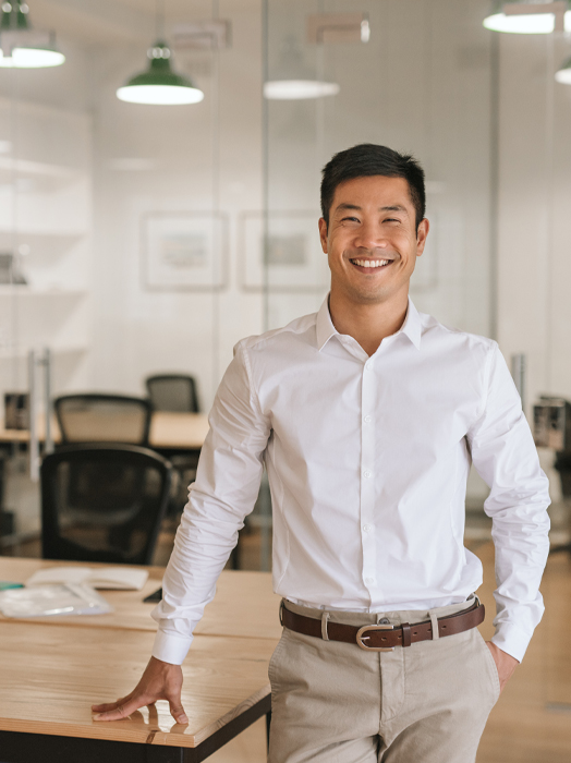 Photo shows a young Asian office worker leaning on a desk.