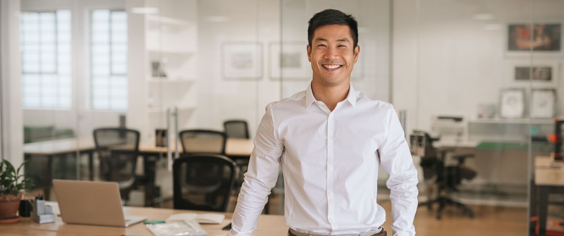 Photo shows a young Asian office worker leaning on a desk.