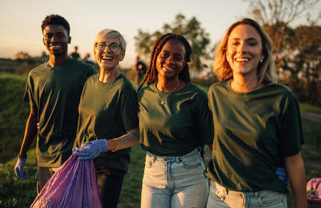 Photo shows 4 diverse people outside wearing matching green tshirts as they collect rubbish together.