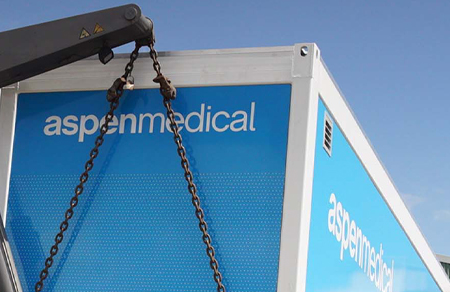Photo shows an Aspen Medical mobile health unit being hoisted up onto a truck for transportation.