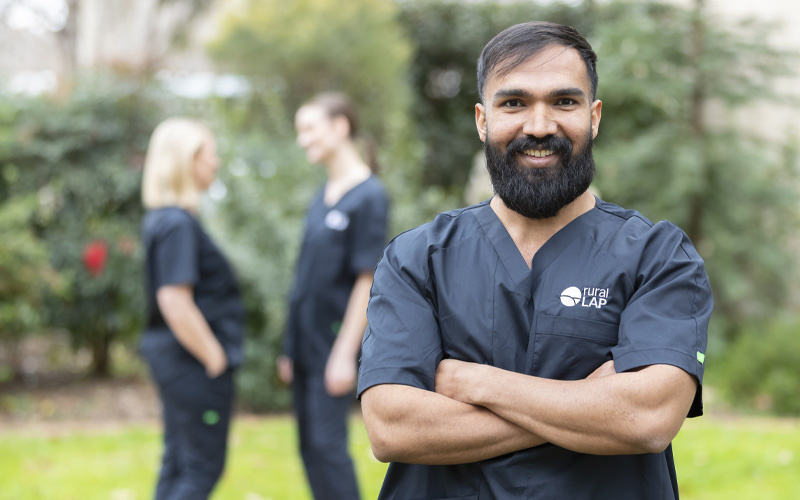 Photo of a male Rural LAP clinician smiling with arms crossed, wearing branded dark blue scrubs.