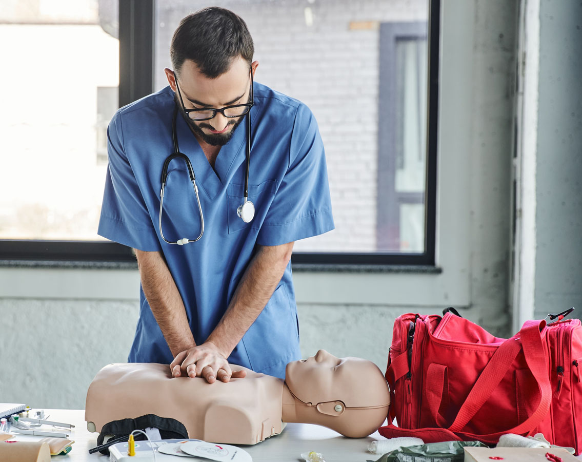 Photo shows a male Emirati clinician in glasses practicing CPR on a dummy.
