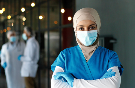 Photo shows a young Emirati clinician wearing a mask and head scarf.