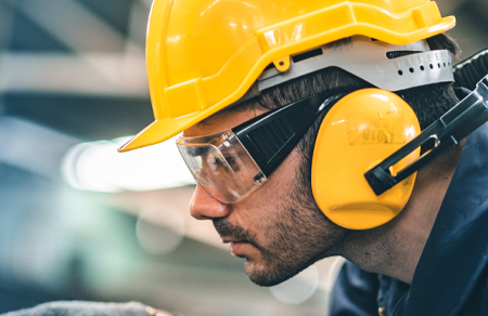 Photo shows an energy sector worker wearing a yellow hardhat, ear covers, eye protection and gloves to operate machinery.