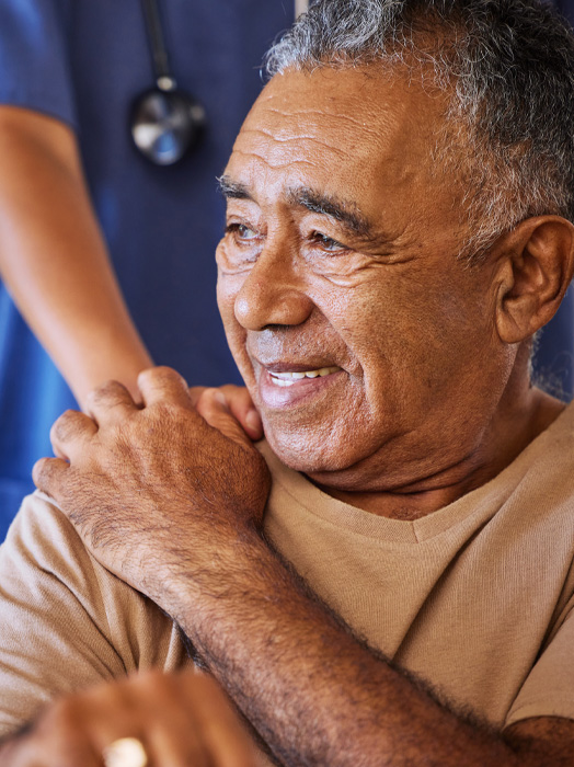 Image shows an elderly man up close with a clinicians hand on his shoulder in support.