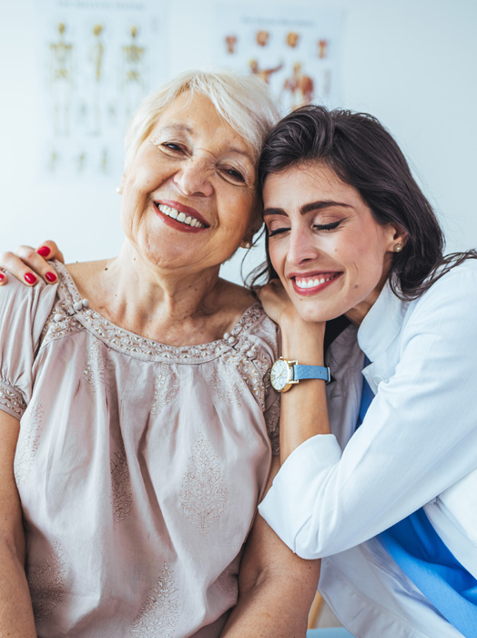 Photo shows a female clinician embracing an elderly patient with affection.