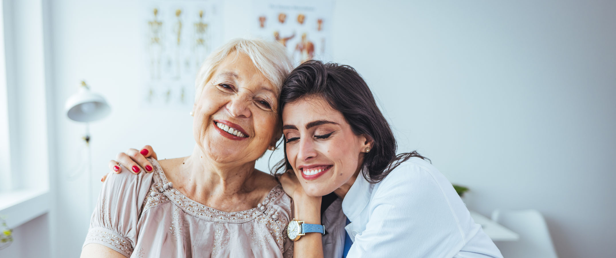 Image shows a female clinician embracing an elderly patient with familiarity.