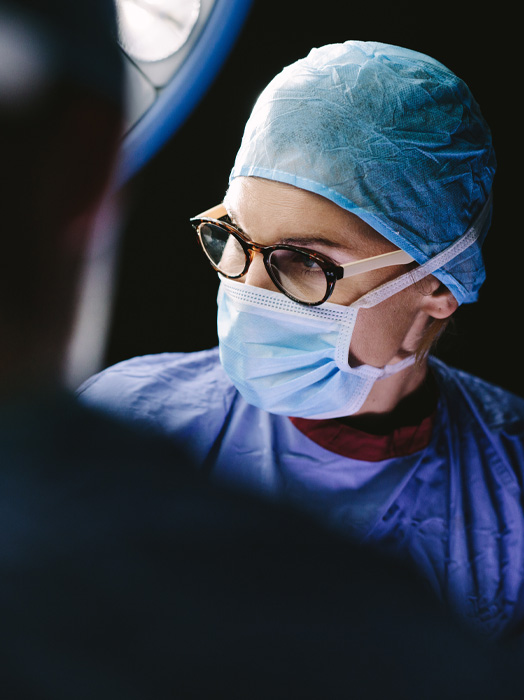 Photo shows a surgeon in full surgical gear with glasses close up.