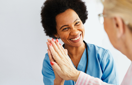 Photo shows a female clinician with dark hair holding the hand of an elderly patient.