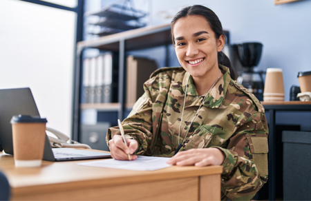 Photo shows a young female soldier sitting at a desk.