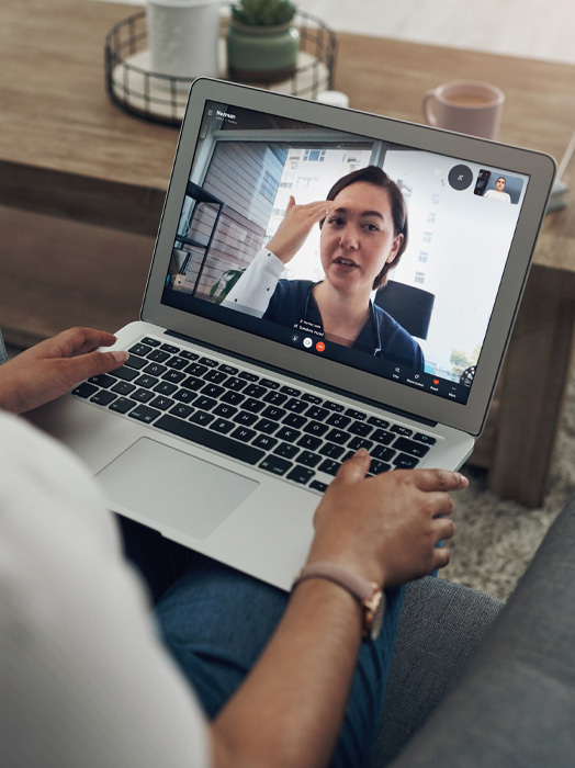 Photo shows a clinicians face on a laptop screen as they interact with a patient holding the laptop.