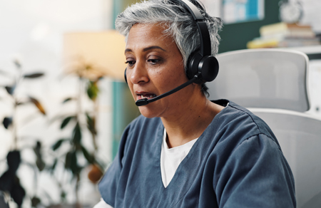 Image shows a female virtual care clinician taking a call on a headset.