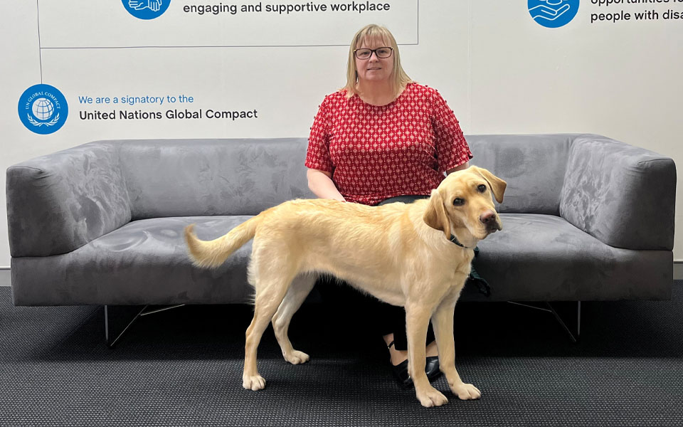 Photo of Kelly-Ann sitting on the couch in Canberra reception with Lizzy the dog standing infront of her.