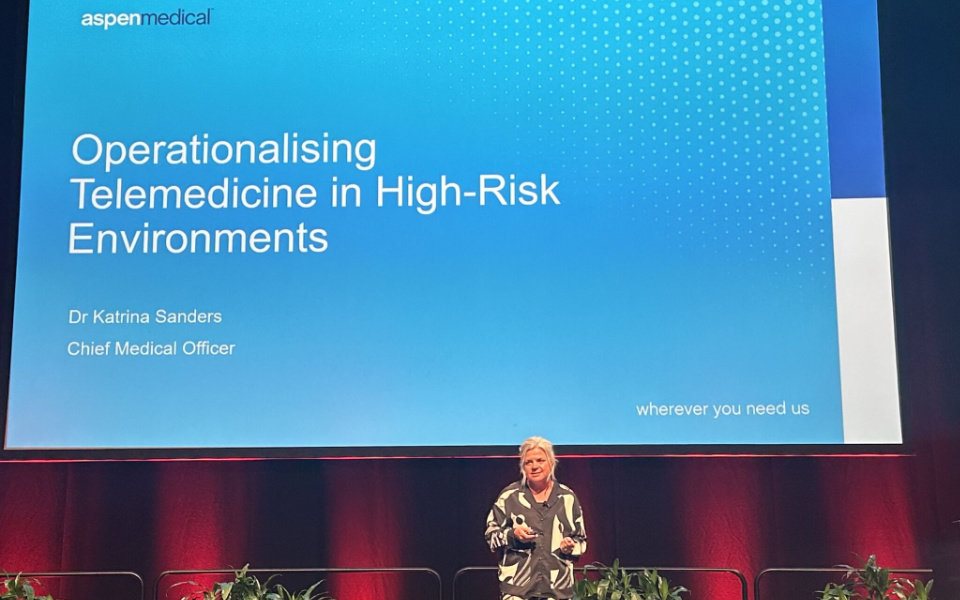 Woman on stage in front of a branded slide presenting at a conference 