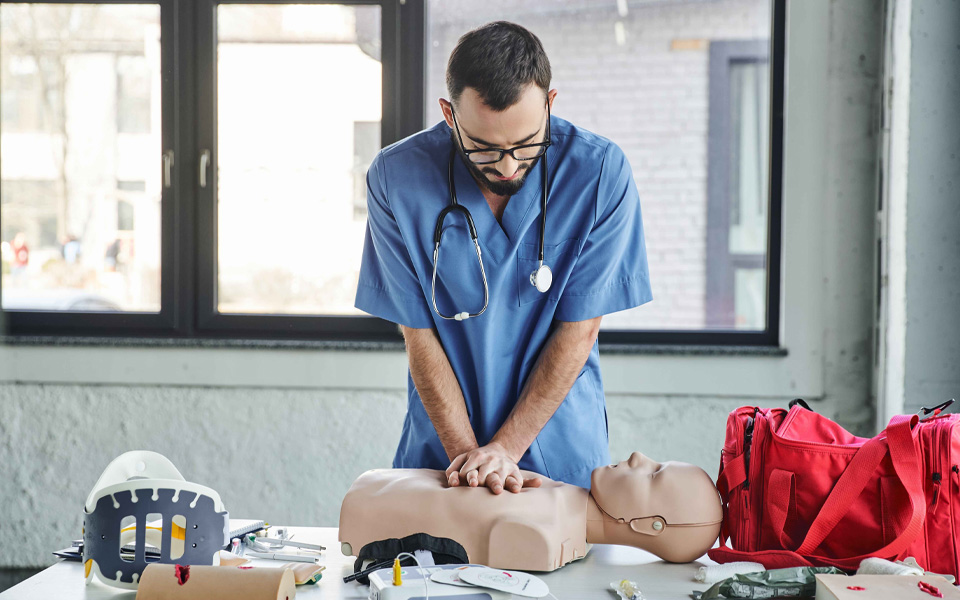 Image shows a male clinician practicing CPR on a dummy.