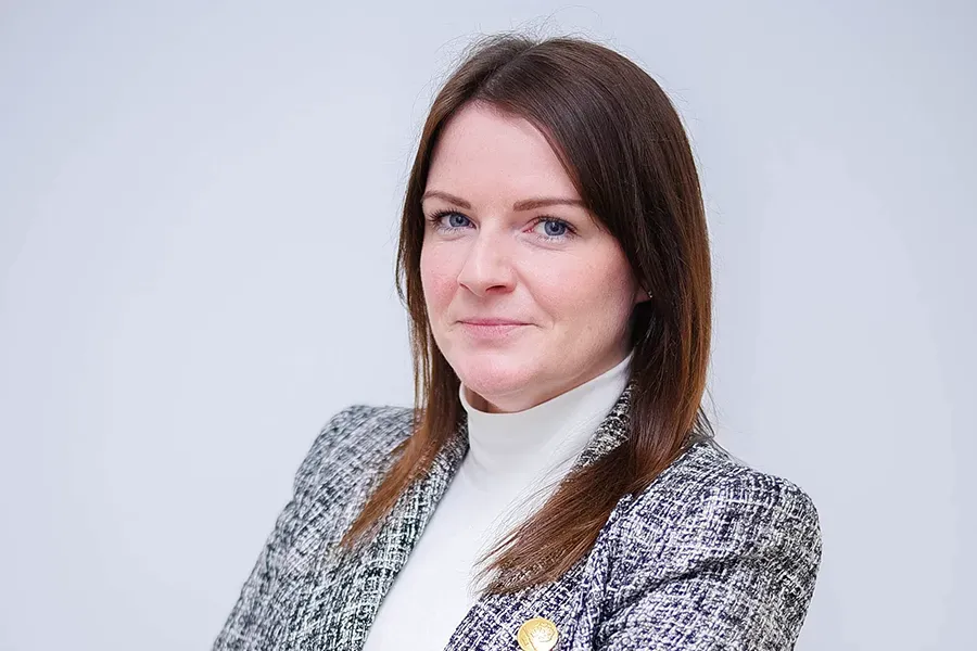 Claire Westbrook-Keir, General Manager of the UAE at Aspen Medical, wearing a white turtleneck top and a grey textured blazer, standing against a plain light background with arms crossed.