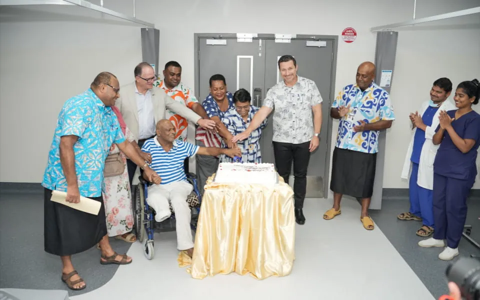 Hospital team of clinicians and executives cutting cake in a ward
