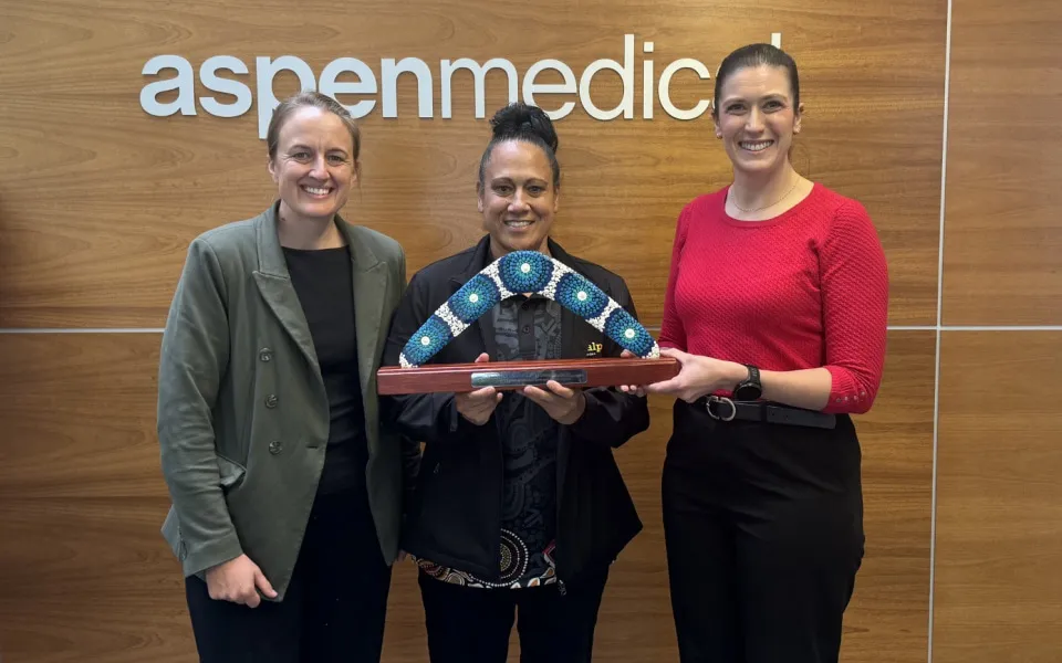 Three women standing against a branded corporate logo on a wall