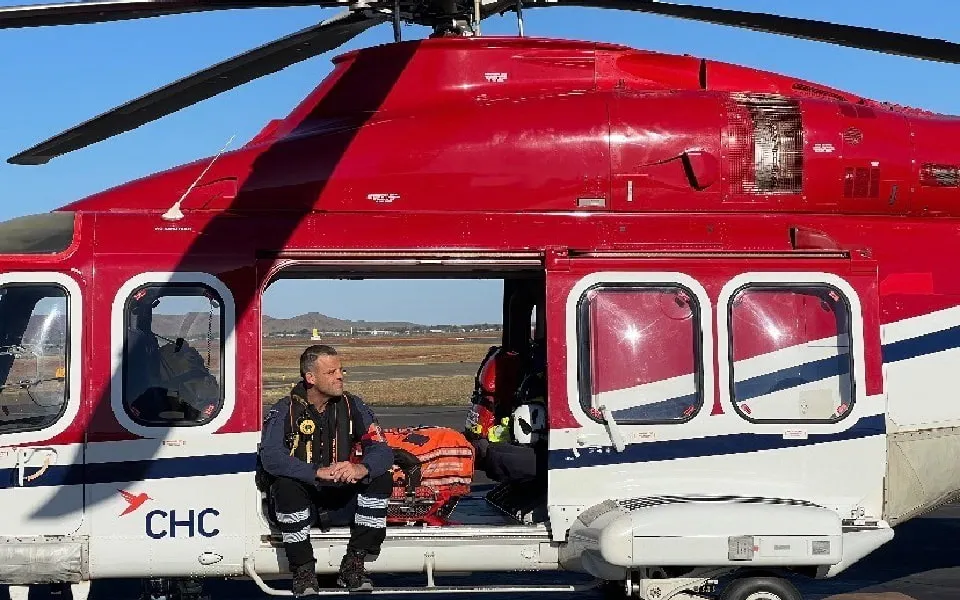 Man in aviation jump suit sitting on side of helicopter with door open 